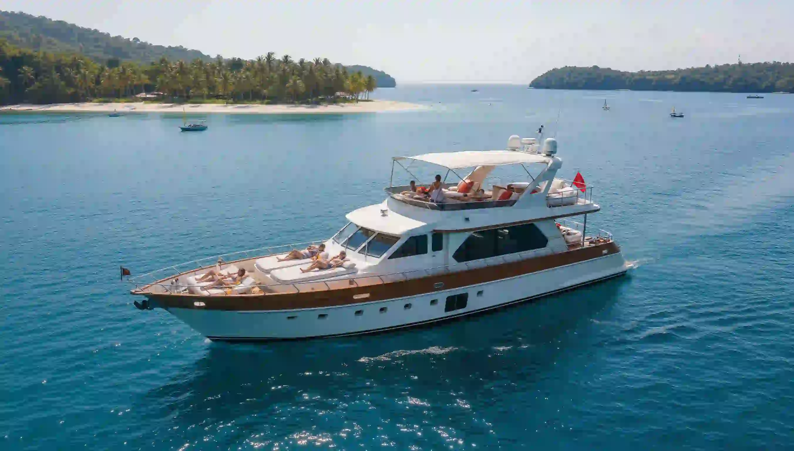 A charter yacht at rest off a palm-fringed island, guests on the foredeck